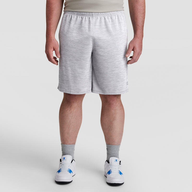 A person wears Champion 10" Moisture Wicking Sport Shorts - Big & Tall in light gray, paired with gray socks and white sneakers with blue accents, standing against a plain light background. Their upper body is partially visible.