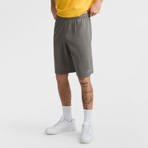 A person stands on a plain white background wearing a yellow shirt and Champion 10" Moisture Wicking, Sport Shorts for men. Their hands are in their pockets, tattoos cover their lower legs, and they complete the look with white socks and sneakers.