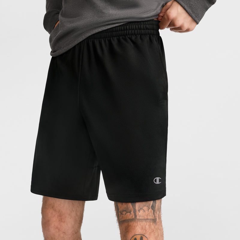 A person wears Champion 10" Moisture Wicking Sport Shorts in black, paired with a gray long-sleeve shirt. The shorts display the Champion logo and provide moisture-wicking comfort. Part of a leg tattoo is visible against a plain white background.