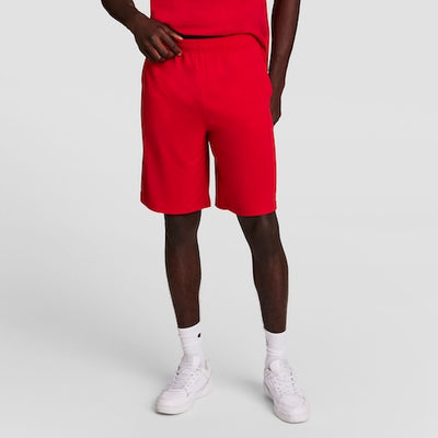 A person wearing a red T-shirt and red shorts stands against a plain light background. They are also wearing white socks and white sneakers. Their head is not visible in the image.