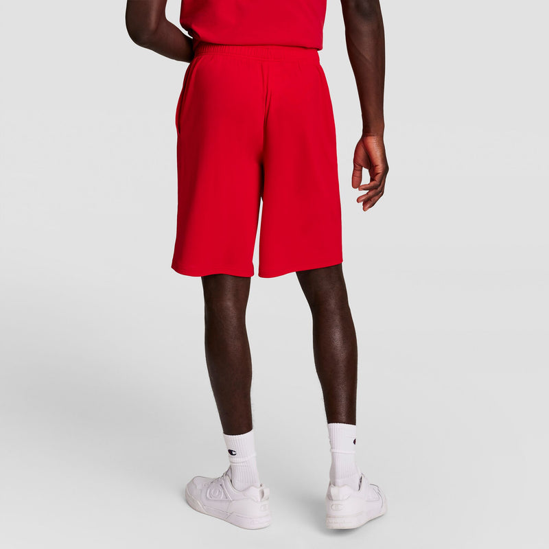 A person stands facing away, wearing Champion 10" Moisture Wicking Sport Shorts in bright red, a matching red shirt, white crew socks, and white sneakers against a plain light gray background.