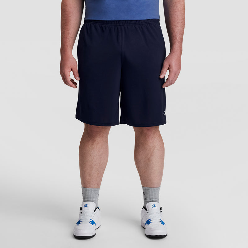 A man stands facing forward against a plain white background, wearing a blue shirt, gray socks, white sneakers, and Champion 10" Moisture Wicking Sport Shorts - Big & Tall. His head is not visible in the image.
