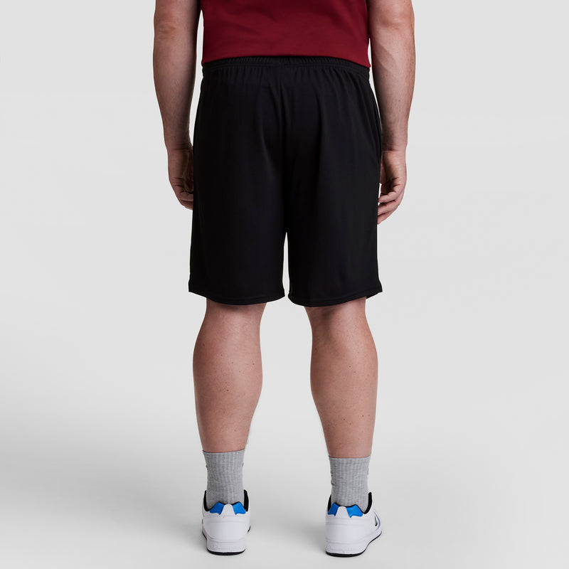 A person stands with their back to the camera, wearing a maroon shirt, gray socks, white sneakers with blue accents, and Champion 10" Moisture Wicking, Sport Shorts - Big & Tall against a plain light background.