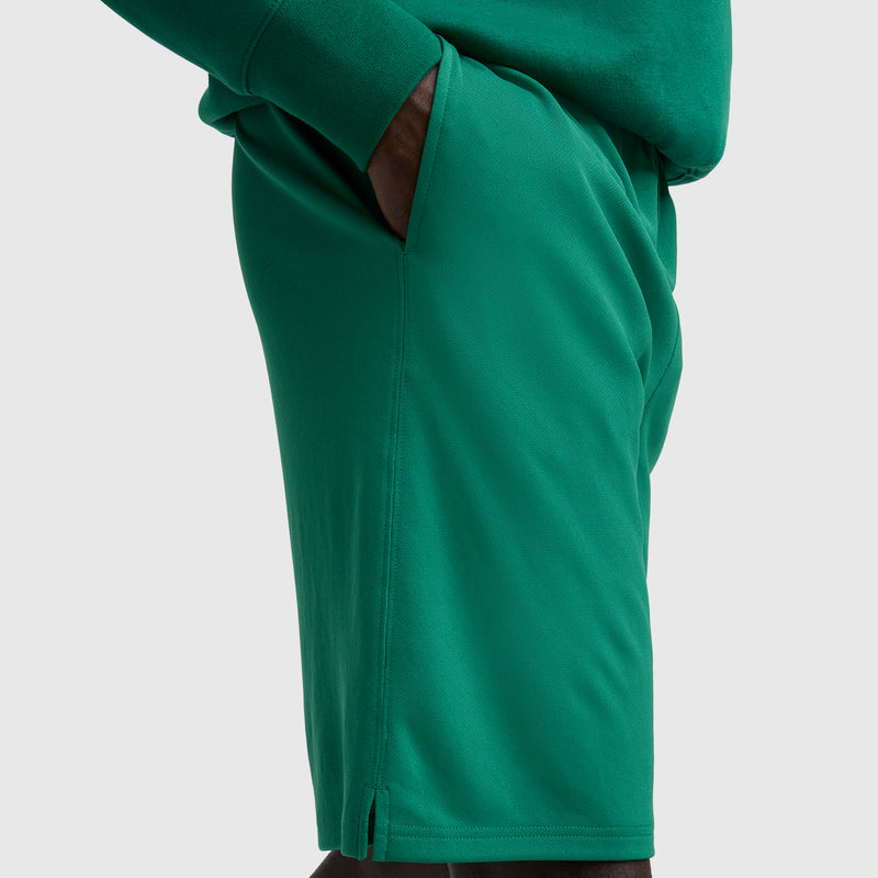 A person models Champion's 10" Moisture Wicking Sport Shorts in bright green, with a matching top and their right hand in their pocket, shown from the side against a plain light background.