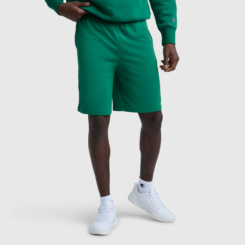 A person wearing 10" Moisture Wicking, Sport Shorts by Champion in green, a matching green sweatshirt, white crew socks, and white sneakers stands against a plain light gray background with their face not visible.