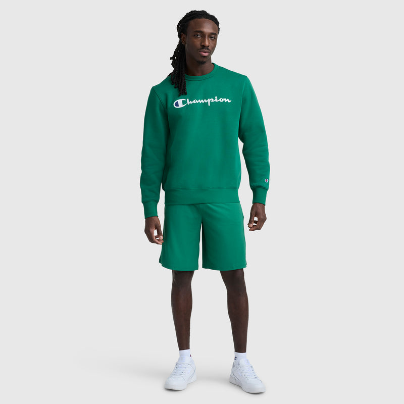 A person stands facing forward wearing a green Champion sweatshirt, Champion 10" Moisture Wicking Sport Shorts, and white sneakers against a plain white background.