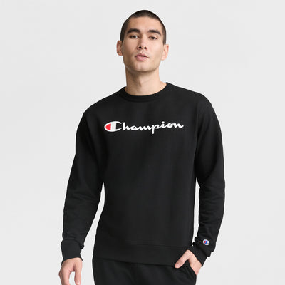 A person stands against a plain background wearing the Champion Powerblend Crewneck Sweatshirt, Classic Script Logo, featuring the Champion logo on chest and sleeve for signature style and comfort.