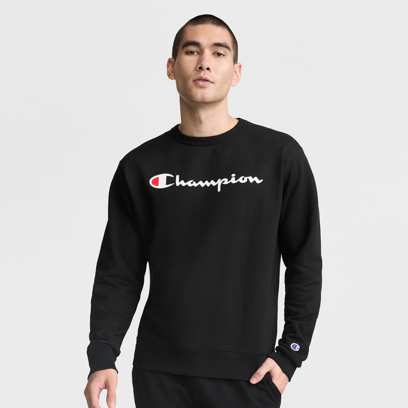 A person stands against a plain background wearing the Champion Powerblend Crewneck Sweatshirt, Classic Script Logo, featuring the Champion logo on chest and sleeve for signature style and comfort.