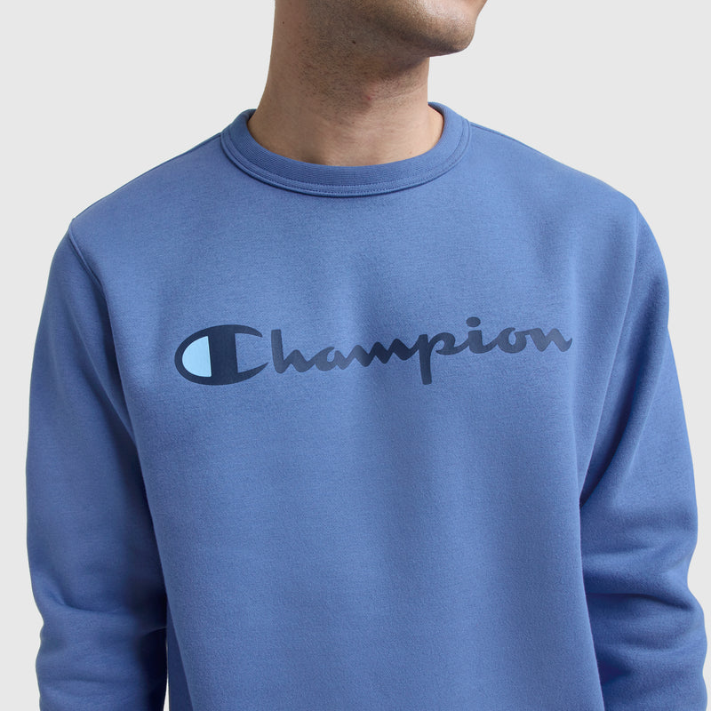 A person wears the Champion Powerblend Crewneck Sweatshirt, featuring the classic script logo in large, bold letters across the chest, shown from shoulders to chin against a plain background.