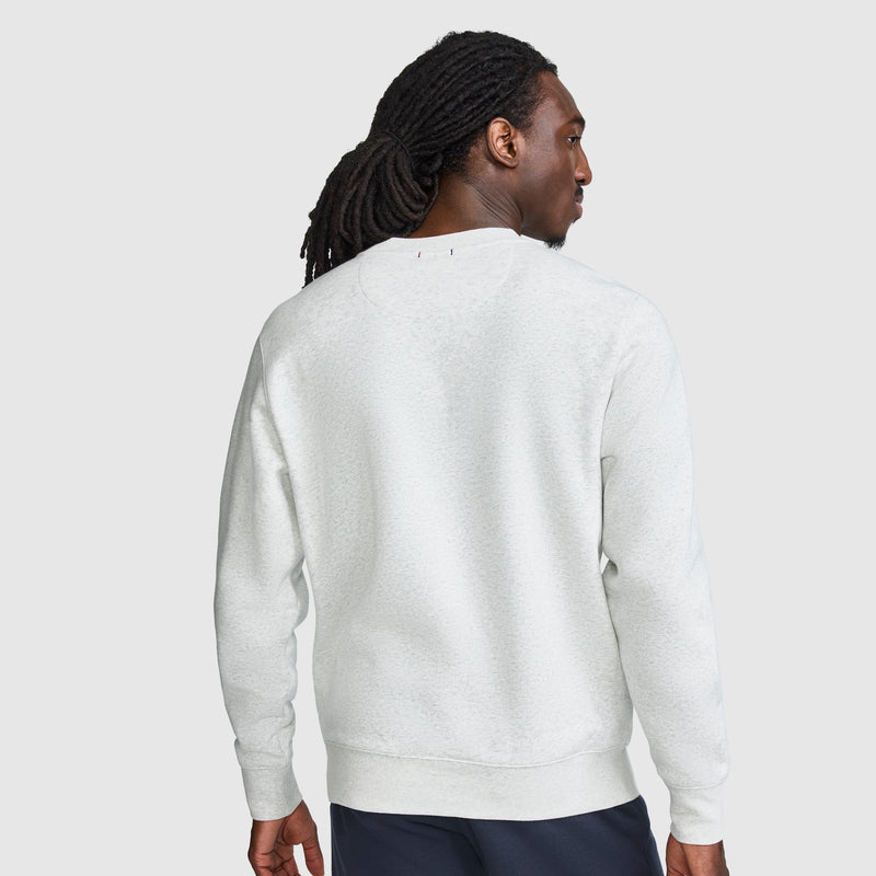 A person with long hair is shown from the back against a light gray background, wearing dark pants and the Champion Powerblend Crewneck Sweatshirt, Tonal Script Logo.