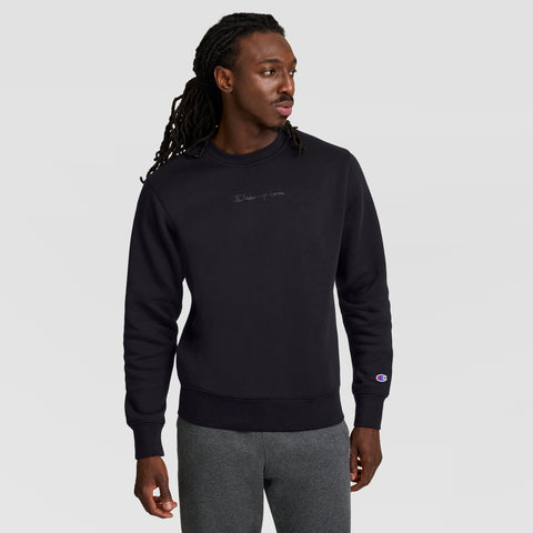 A man with long, braided hair wears the Champion Powerblend Crewneck Sweatshirt with a tonal script logo and gray pants, standing against a light gray background as he looks to his left, showing the classic comfort of this men's sweater.