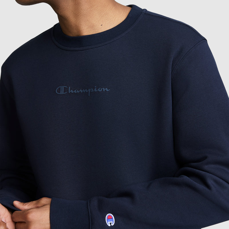 A person is wearing the Champion Powerblend Crewneck Sweatshirt, Tonal Script Logo, featuring an embroidered logo on the chest and a small logo patch on the sleeve. Made from soft Powerblend fleece, this men’s sweatshirt by Champion combines comfort and style. The person’s face is not visible.