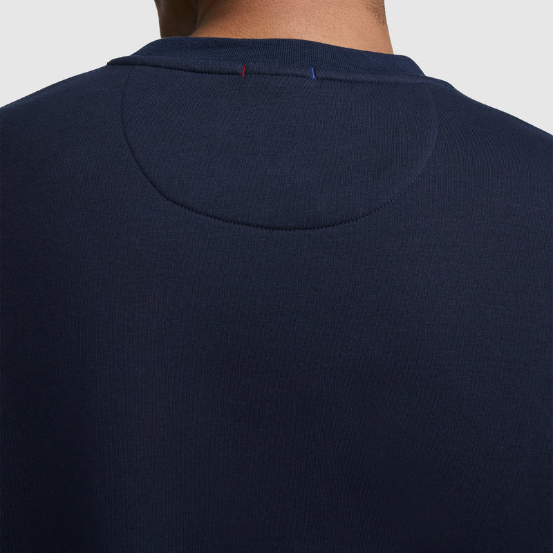 A close-up of the back of the Champion Powerblend Crewneck Sweatshirt, Tonal Script Logo, in navy blue showcases a small stitched oval detail near the collar and a visible red and blue stitch at the neck seam. This men’s sweatshirt is made with soft Powerblend fleece for enhanced comfort and durability.