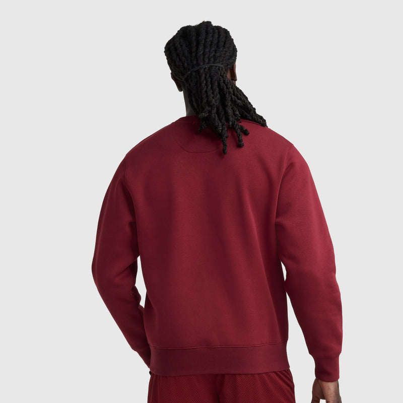 A person with long, twisted hair is seen from the back wearing a maroon Champion Powerblend Crewneck Sweatshirt, C Logo, and matching shorts against a plain light gray background.