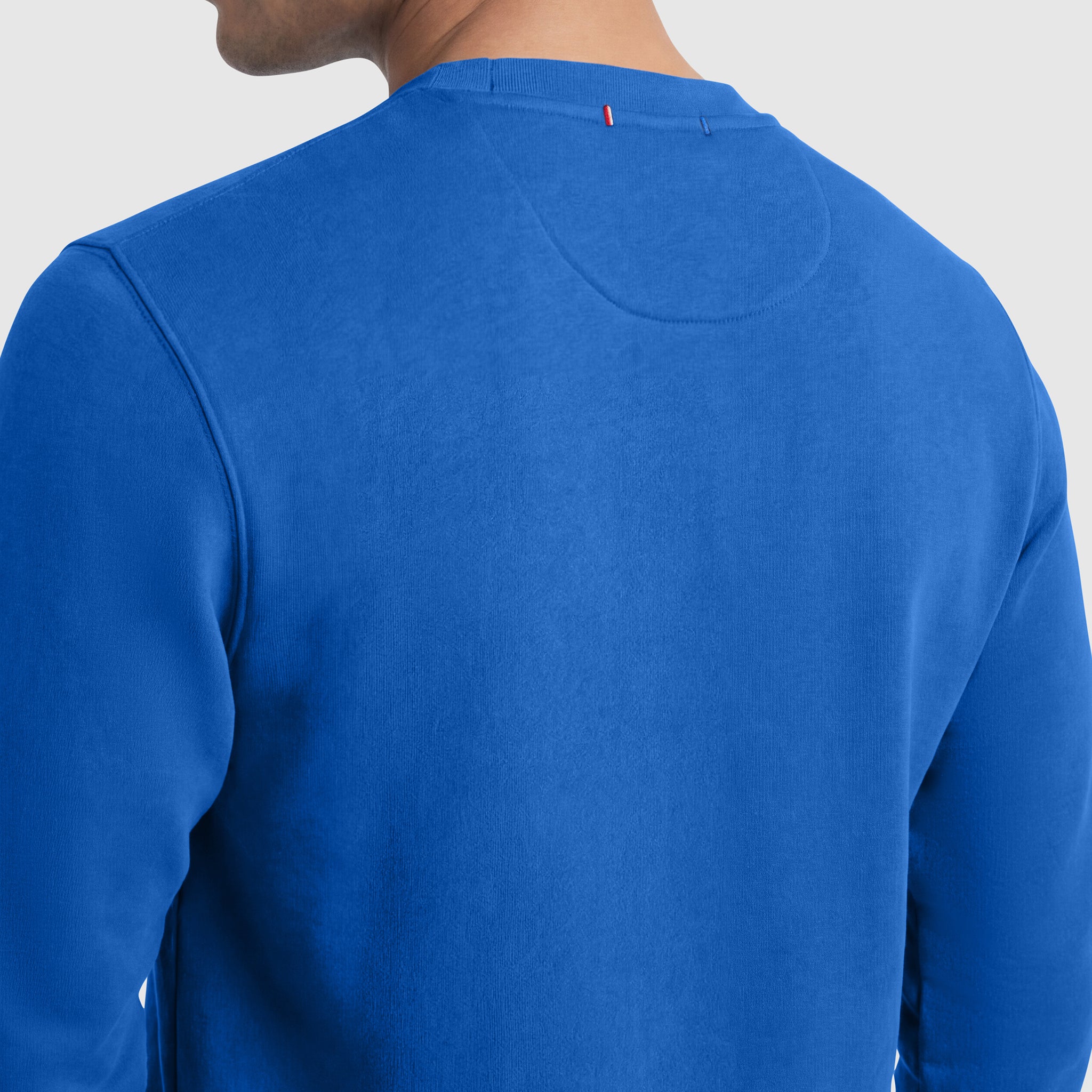 A person is seen from the back wearing a Champion Powerblend Crewneck Sweatshirt, C Logo. Only the neck, shoulders, and upper back of the men's pullover are visible against a plain gray background.