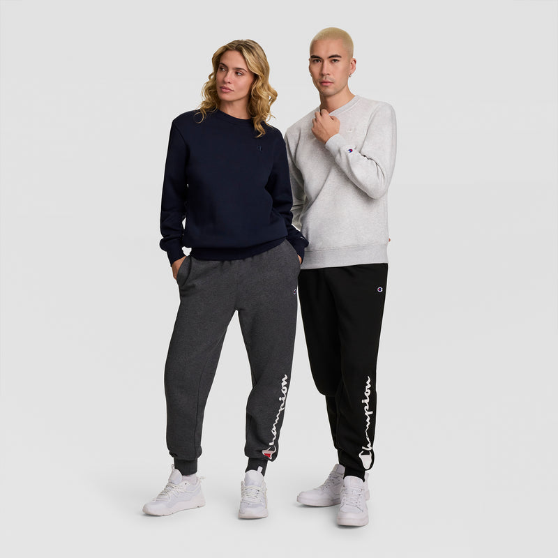 Two people stand side by side wearing casual Champion outfits. The person on the left sports a Champion Powerblend Crewneck Sweatshirt, C Logo in navy and dark gray, while the person on the right opts for a light gray and black Champion men’s sweatshirt crafted from soft athletic fleece. Both wear white sneakers.