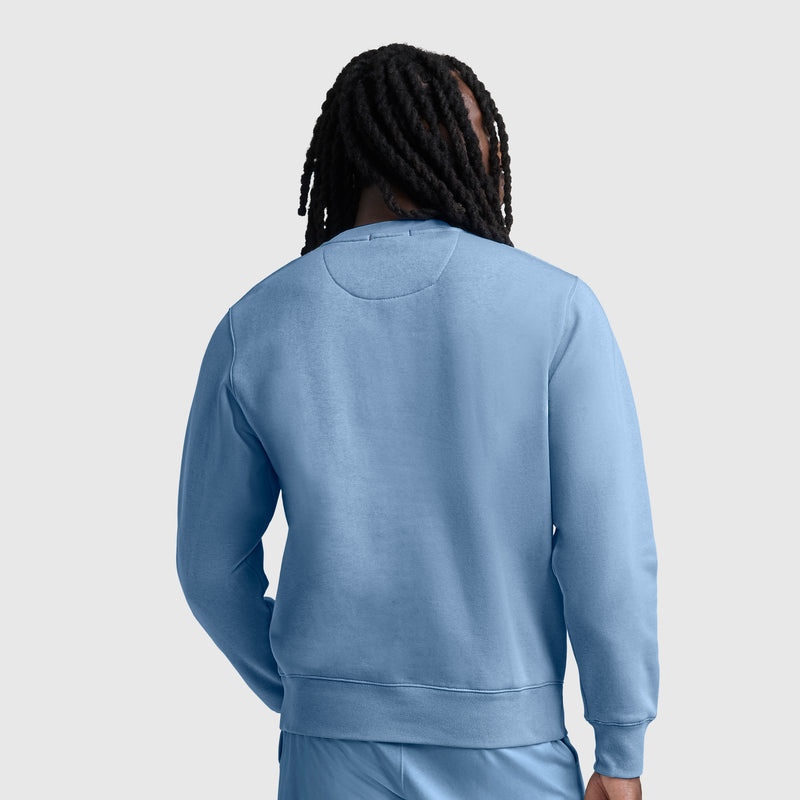 A person with long dreadlocks is shown from behind, wearing a light blue Champion Powerblend Crewneck Sweatshirt with the C logo and matching athletic fleece pants against a plain light gray background.