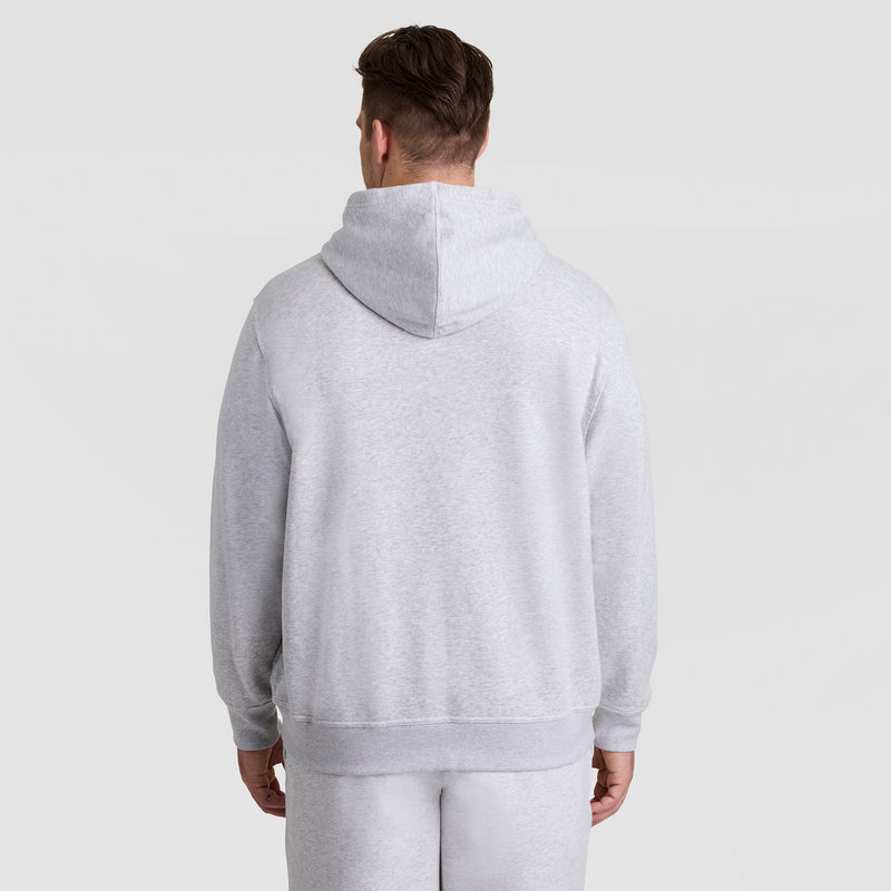 A person stands with their back to the camera against a plain light background, wearing a light gray Champion Powerblend Hoodie, Full Script Logo - Big & Tall, paired with matching sweatpants.