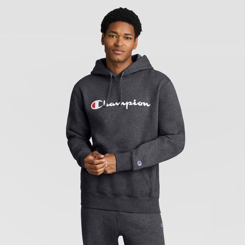 Wearing a dark gray Champion Powerblend Hoodie with the Full Script Logo and matching sweatpants, a person stands against a plain light gray background, looking at the camera with a neutral expression.