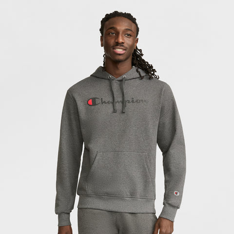 A man wearing a gray Champion Powerblend Hoodie, Full Script Logo, stands smiling against a white background. The midweight hoodie features the Champion script across the chest and a small sleeve logo.