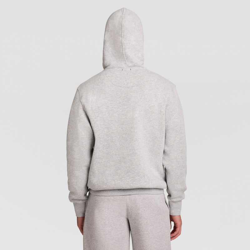 A person is shown from the back with the hood up, wearing the Champion Powerblend Hoodie, Full Script Logo in light gray along with matching sweatpants, standing against a plain white background.
