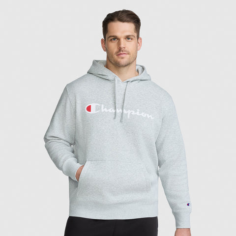 A man wears a heather gray midweight Champion Powerblend Hoodie, Full Script Logo - Big & Tall, with a large logo across the chest and a hand in the front kangaroo pocket.
