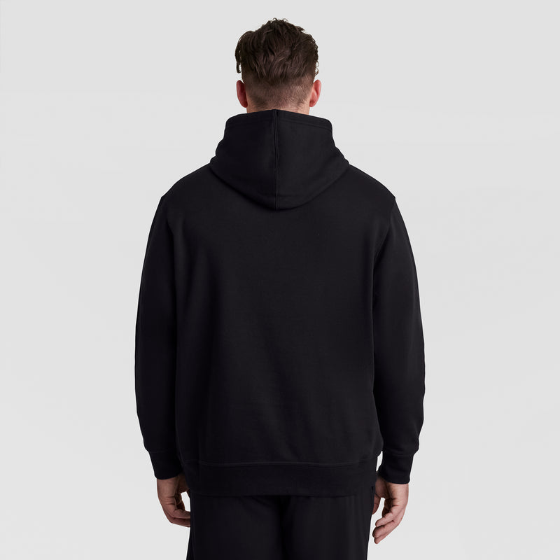 A person with short brown hair is shown from the back, wearing the Champion Powerblend Hoodie, Full Script Logo - Big & Tall in black, along with black pants, standing against a plain light gray background.