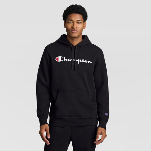 A man stands facing forward against a plain gray background, wearing a black Champion Powerblend Hoodie with the full script logo displayed on the front.
