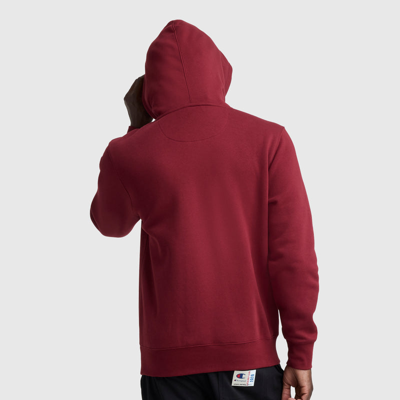A person is seen from the back wearing a red Champion Powerblend Hoodie, Full Script Logo, with the hood up, standing against a plain light gray background.