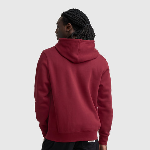 A person with long, twisted hair is seen from the back wearing the Champion Powerblend Hoodie, Full Script Logo in maroon with black pants against a plain light gray background.