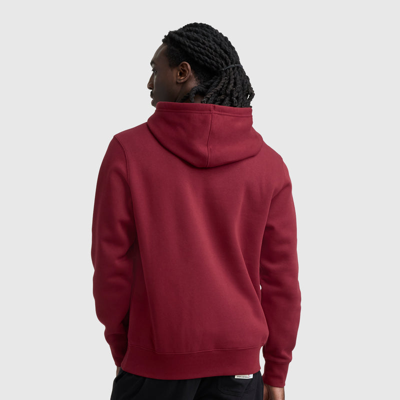 A person with long, twisted hair is seen from the back wearing the Champion Powerblend Hoodie, Full Script Logo in maroon with black pants against a plain light gray background.