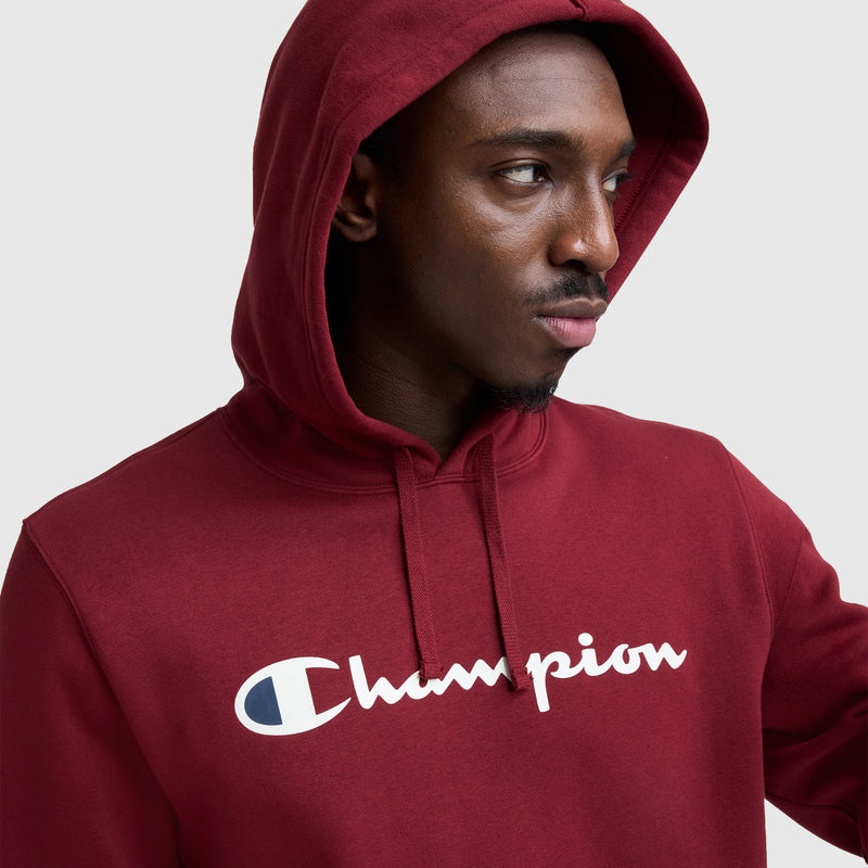 A man wears the Champion Powerblend Hoodie, featuring a full script logo in white across the chest, and gazes to the side against a plain background.