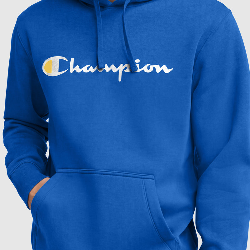 A person wears the Champion Powerblend Hoodie, Full Script Logo—a bright blue men’s fleece pullover with a white Champion logo and yellow-and-white C emblem across the chest. Their left hand rests in the front pocket.