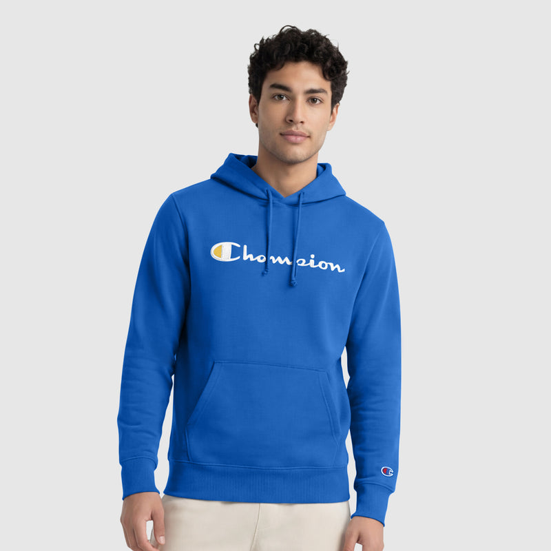 A young man with curly hair wears the Champion Powerblend Hoodie, Full Script Logo, in bright blue, featuring a large logo on the chest, while standing against a plain light gray background.