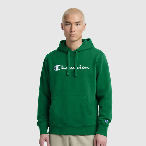 A person with short blond hair wears the Champion Powerblend Hoodie, Full Script Logo—a green men’s fleece pullover with a front pocket and white Champion branding—standing against a plain light gray background.