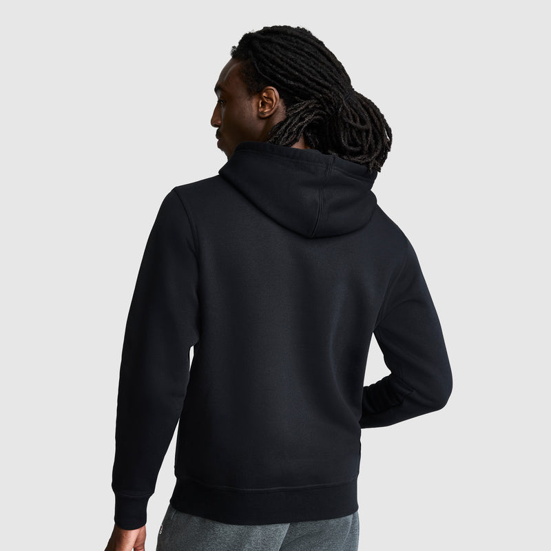 A person with long, dark dreadlocks stands facing away, wearing a black Champion Powerblend Hoodie with a tonal script logo and gray pants against a plain light gray background.