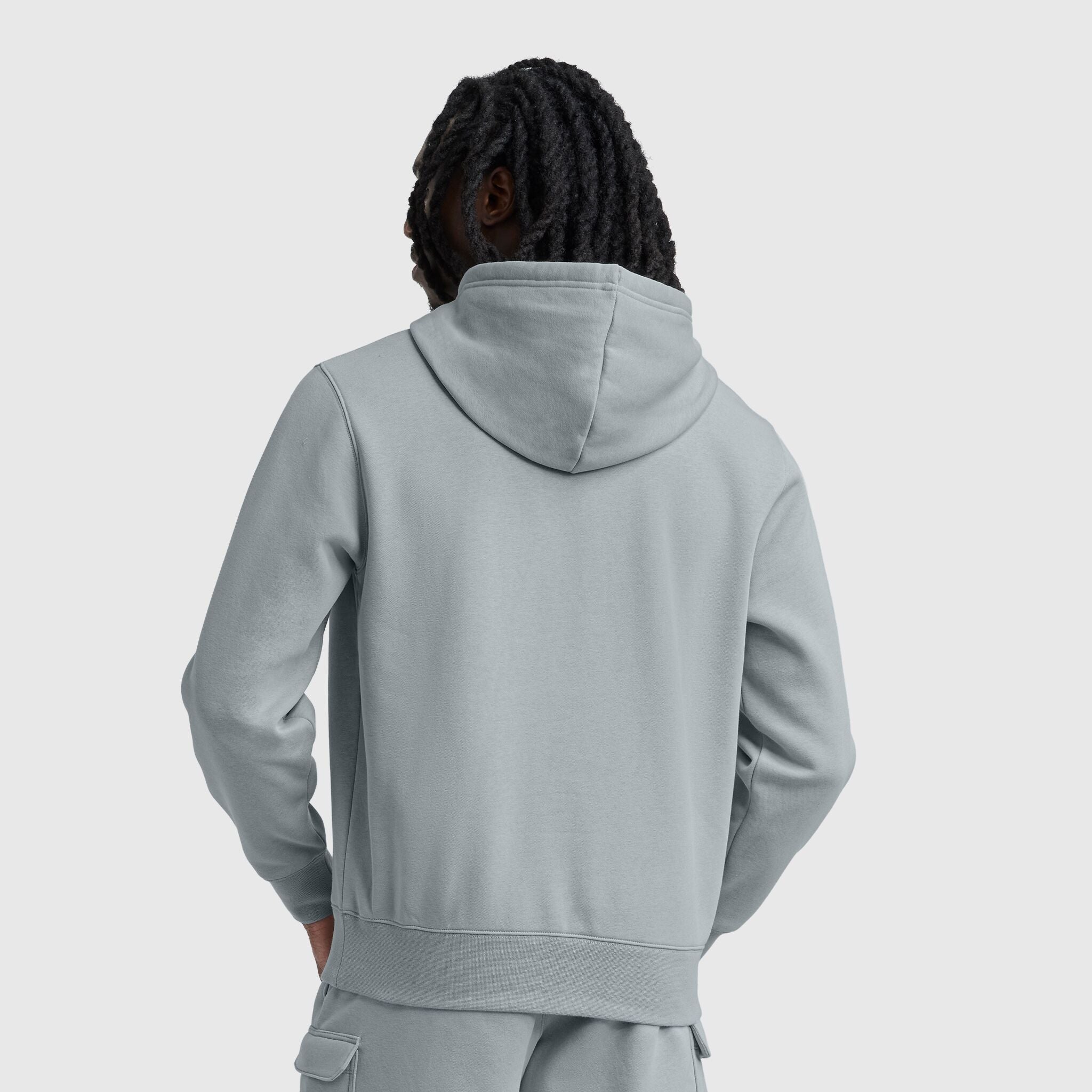 A person with long, dark, twisted hair is seen from behind against a plain light gray background, wearing a Champion Powerblend Hoodie with a tonal script logo and matching pants.