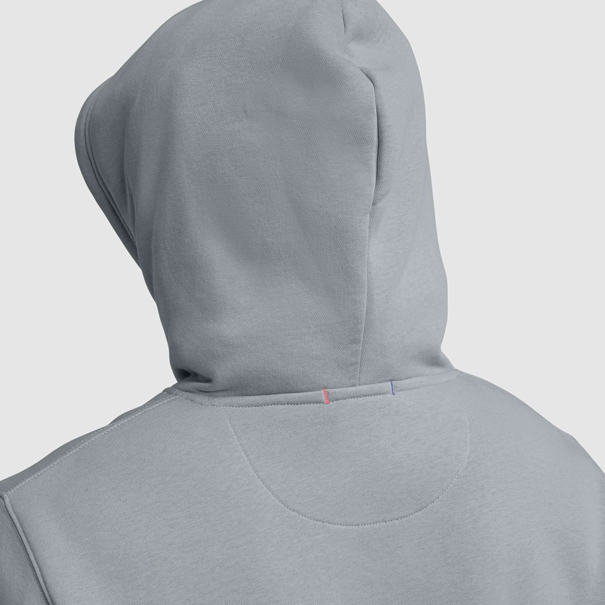 A close-up of the back of a light gray Champion Powerblend Hoodie, Tonal Script Logo, showing the hood and two small stitched lines—one red and one blue—on the neckline, classic details of this style.