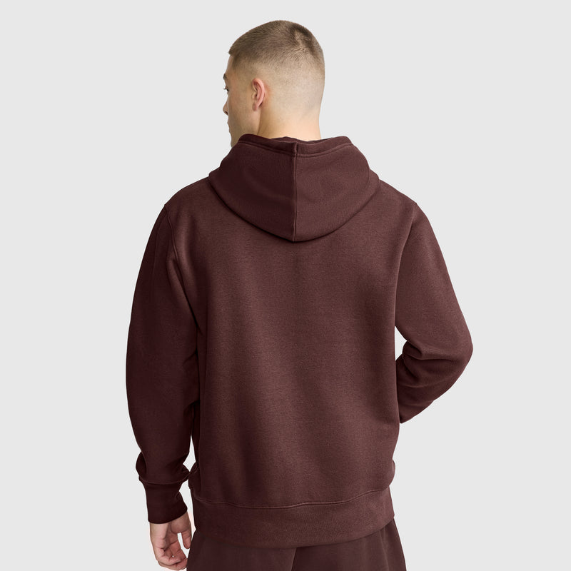 A person with short hair, seen from behind, wears the Champion Powerblend Hoodie with Tonal Script Logo in brown along with matching pants, standing against a plain light gray background.