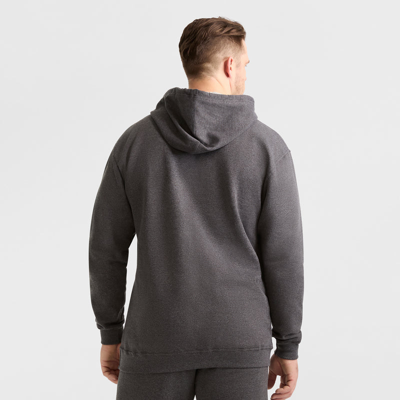 A man faces away from the camera, wearing a Champion Powerblend Hoodie, C Logo - Big & Tall in dark grey with matching pants, set against a plain light background.