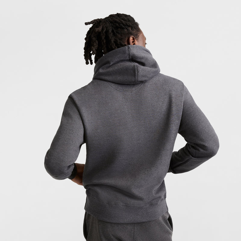 A person with dark, short dreadlocks is seen from behind, wearing a dark gray Champion Powerblend Hoodie, C Logo, with matching pants, against a plain white background.
