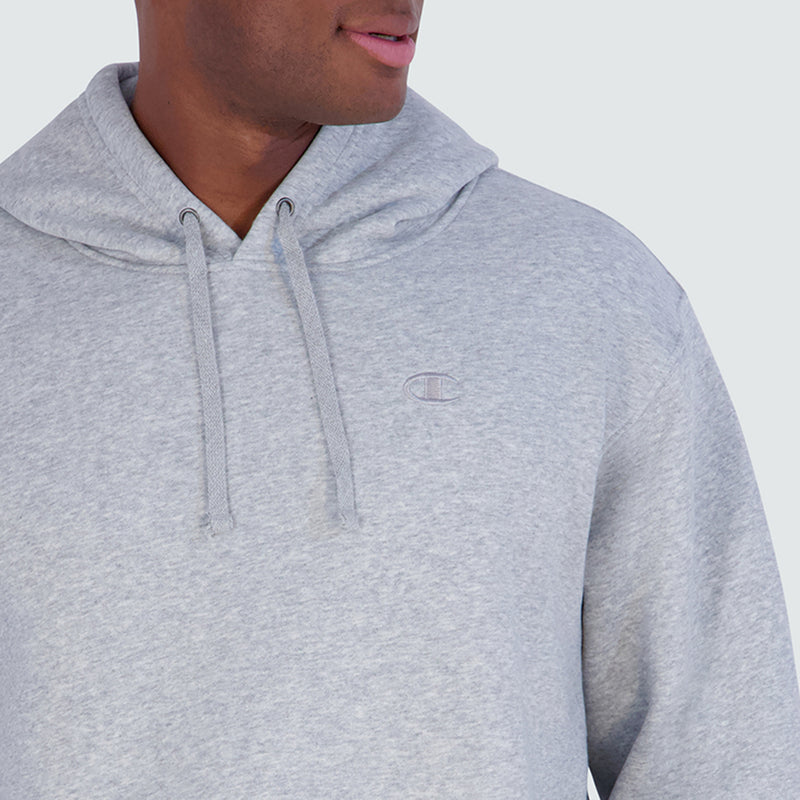 A person wearing a grey Champion Powerblend Hoodie, C Logo - Big & Tall with a small embroidered logo on the chest.