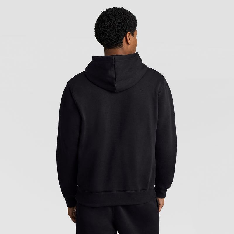 A person wearing a black Champion Powerblend Hoodie, C Logo, and black pants is standing with their back to the camera against a plain light background.