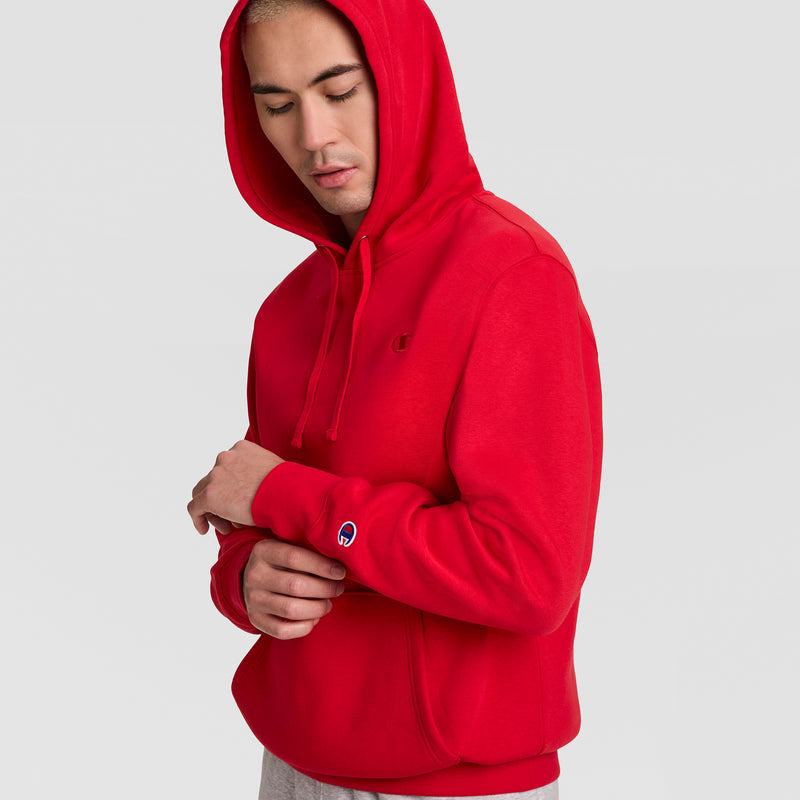 A person wearing a red Champion Powerblend Hoodie, C Logo, with a logo on the chest and a patch on the sleeve.