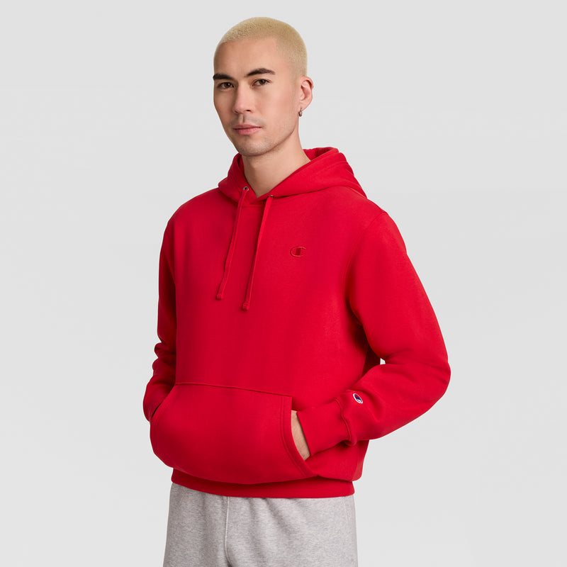 A person wearing a bright red Champion Powerblend Hoodie, C Logo, featuring a front kangaroo pocket and a small logo on the chest and sleeve.