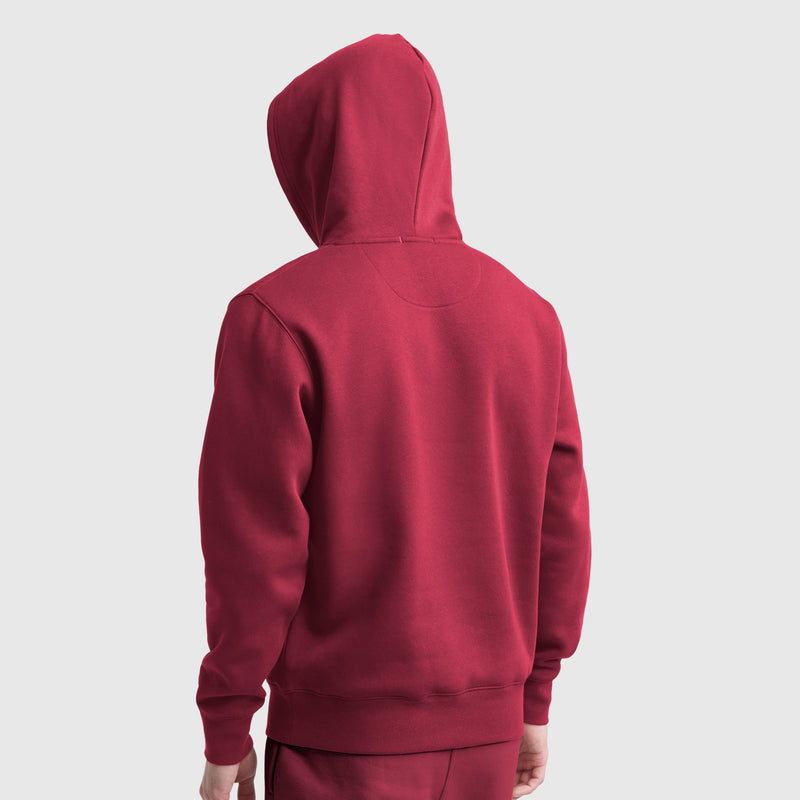 A person wearing a red Champion Powerblend Hoodie, C Logo and matching pants stands with their back to the camera against a plain light gray background.