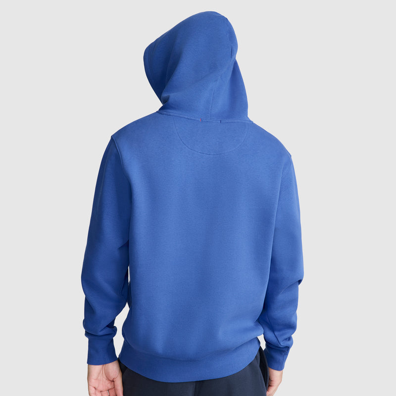 A person is shown from the back wearing a blue Champion Powerblend Hoodie, C Logo, with the hood up and hands at their sides, set against a plain light background.