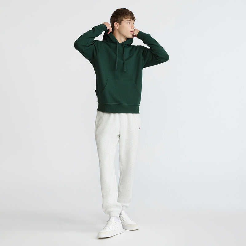 Person wearing a green hoodie and white pants on a white background