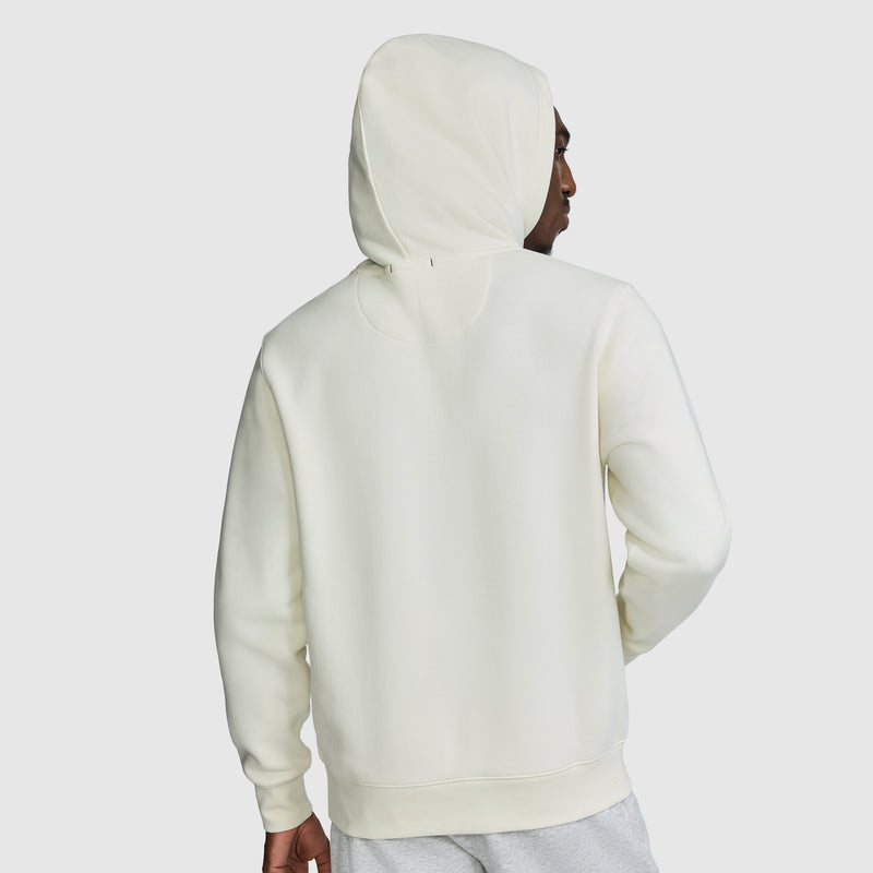 A person wearing a white Champion Powerblend Hoodie with the C Logo stands with their back to the camera, head turned slightly to the side. The background is plain and light-colored.