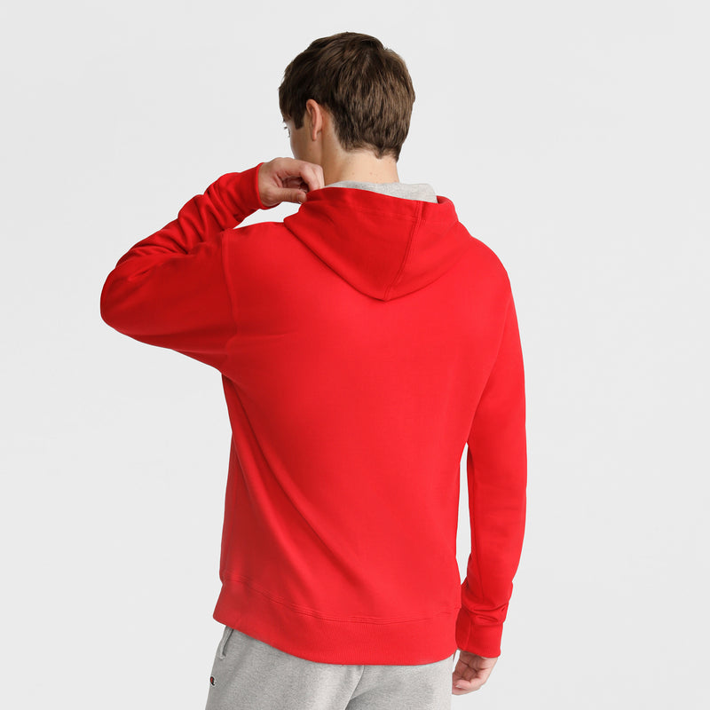A person faces away, wearing a Champion Powerblend Hoodie, C Logo, in bright red with light gray pants. Their hand is raised to their neck against a plain white background.